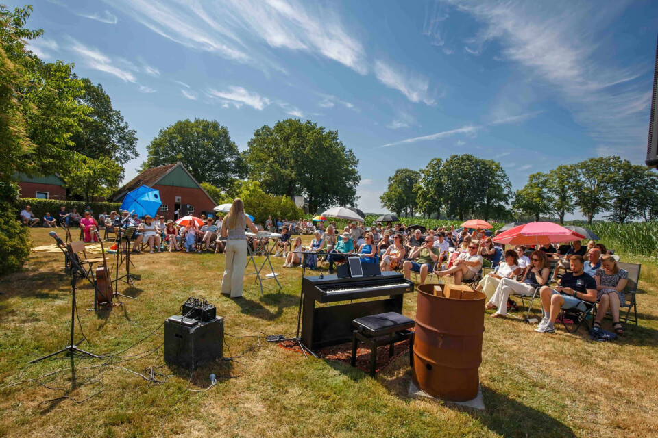 Bezoekers zitten in het gras en op stoelen tijdens een buitendienst van Summer Sundays