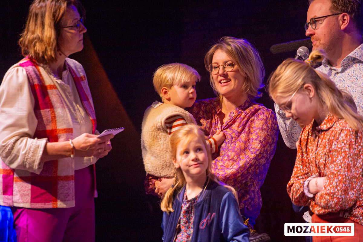 Ouders met hun kinderen op de arm luisteren terwijl er tijdens de opdraagdienst voor hen wordt gebeden