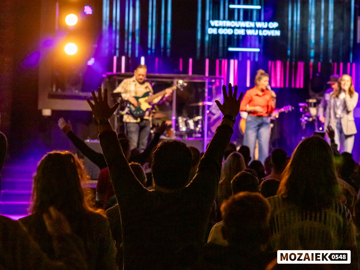 Bezoekers heffen hun handen tijdens de worship terwijl de band op het podium speelt