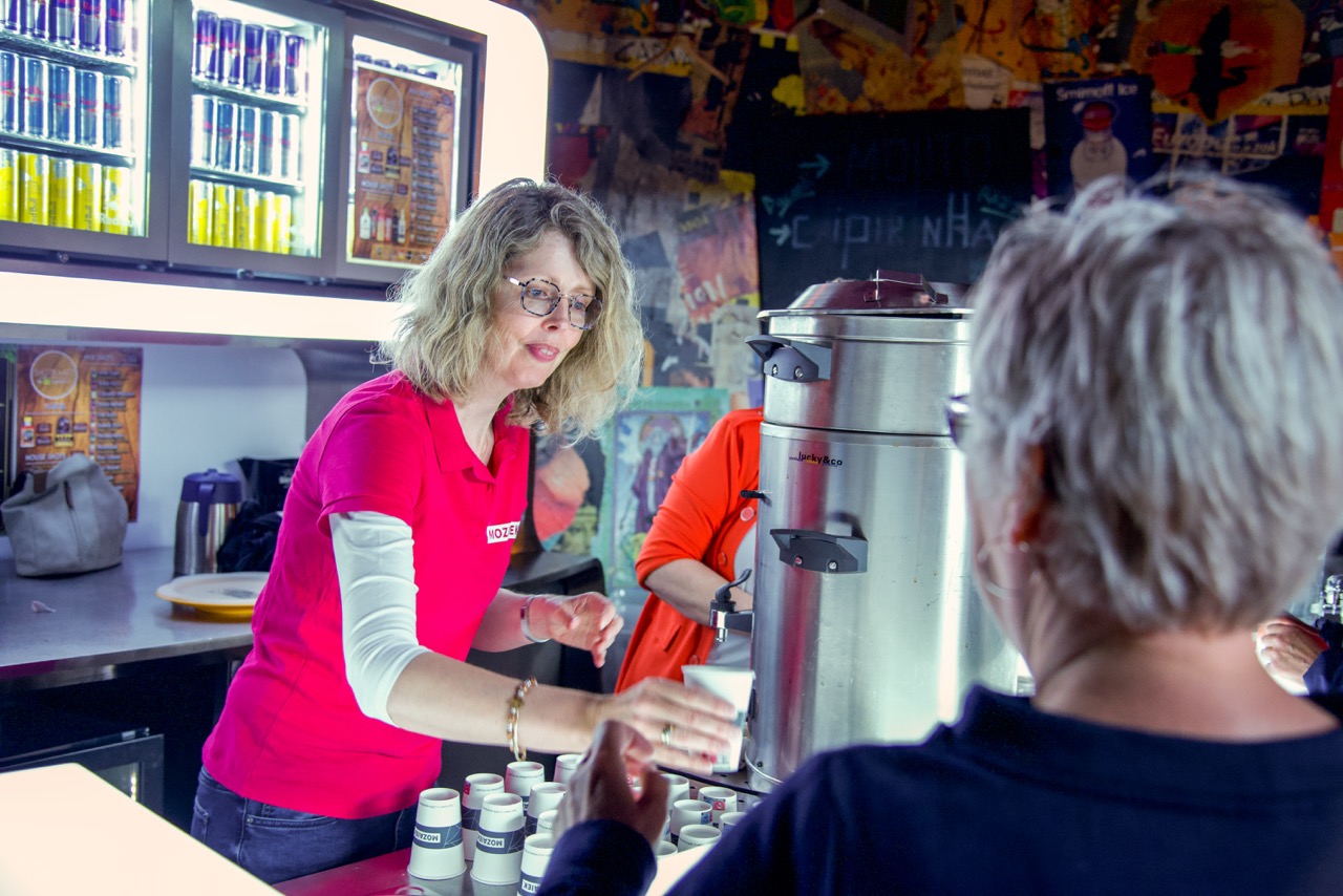 Vrijwilliger schenkt koffie in voor een bezoeker bij de koffiebar