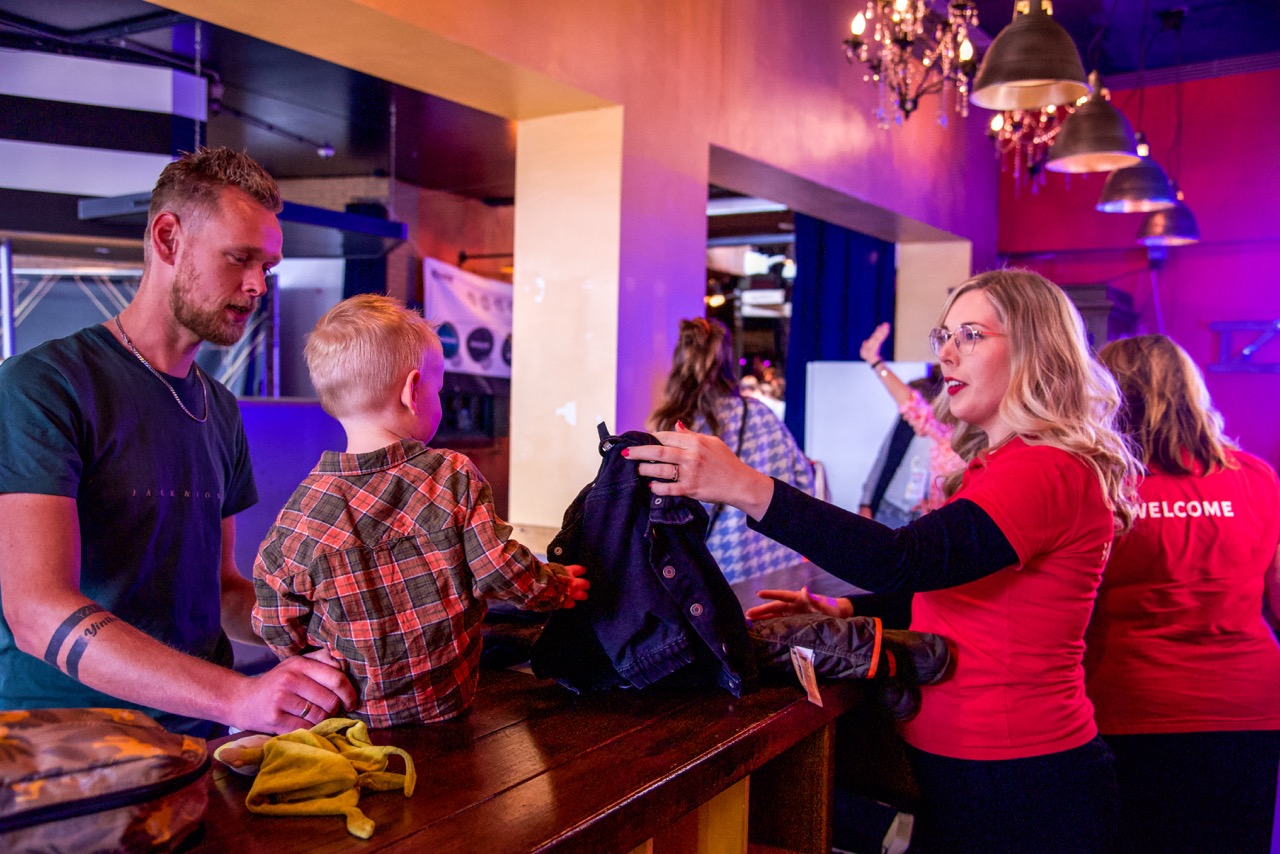 Gastvrouw met welcome-shirt helpt een vader en zijn kind bij de balie