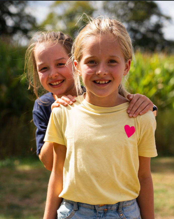 Twee lachende meisjes met een arm om elkaar heen tijdens een activiteit van Mozaiek Kids