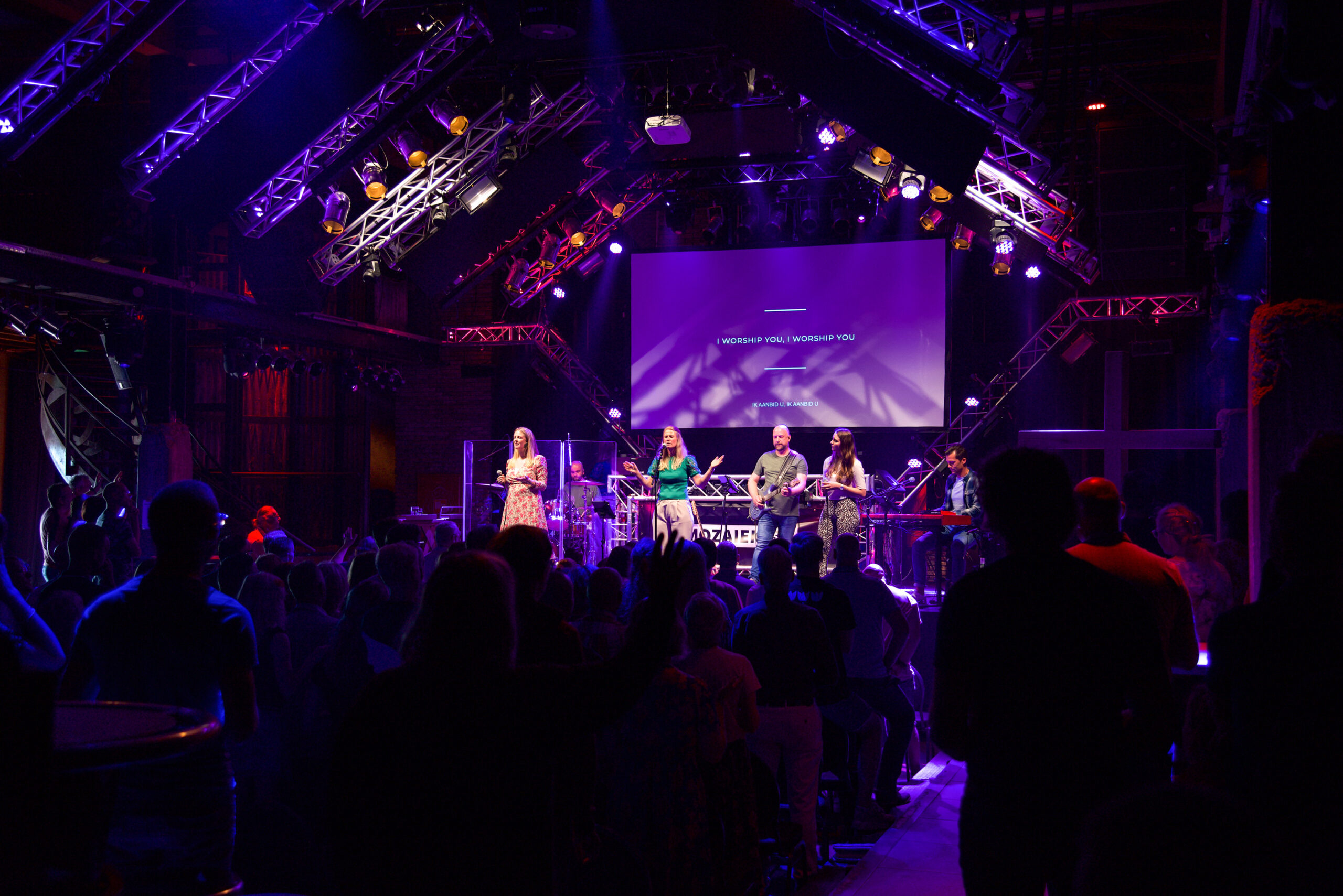 Overzicht van de volle zaal met podium en scherm tijdens de samenkomst