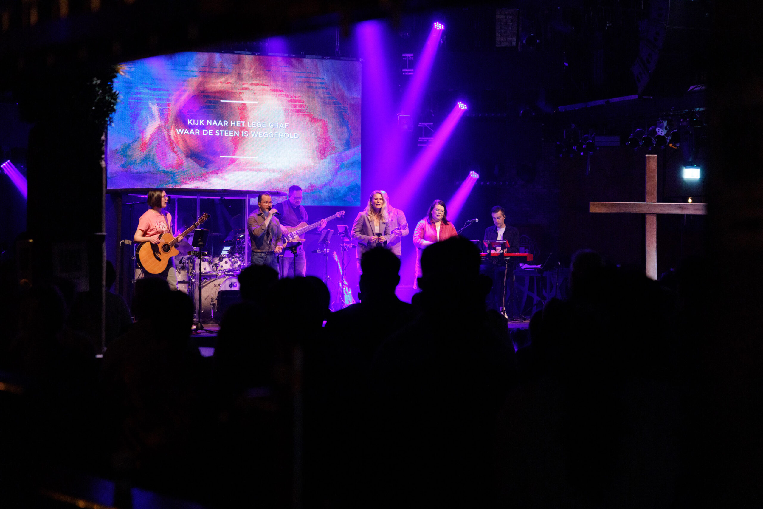 De band speelt op het podium onder paars licht met het houten kruis ernaast