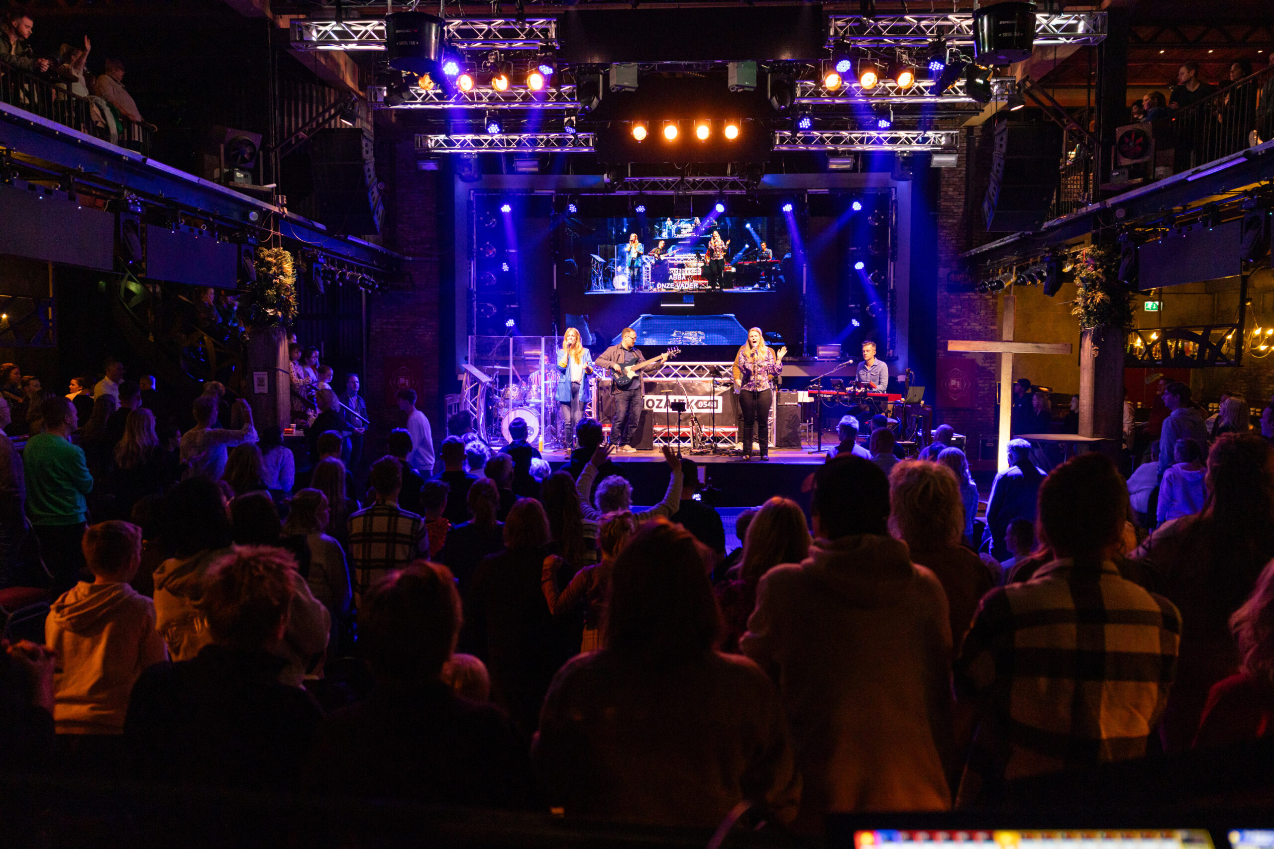 Bezoekers in een volle zaal kijken naar de band op het podium tijdens een dienst van Mozaiek0548