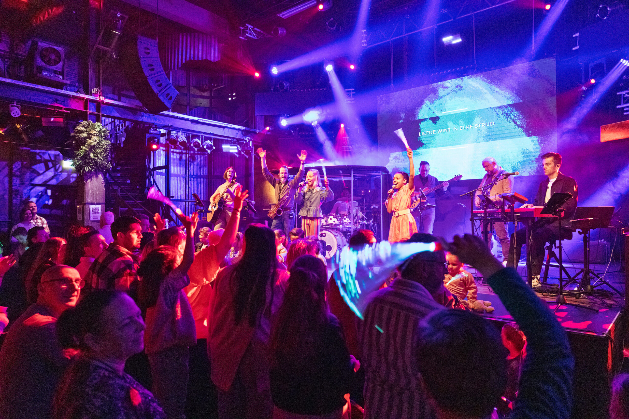 Bezoekers steken hun handen op tijdens de worship terwijl de band speelt