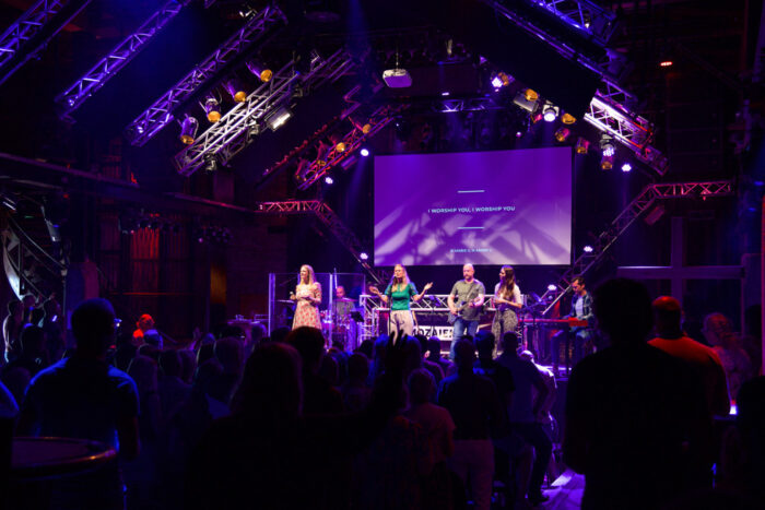 Podium en zaal van Mozaiek0548 in paars licht tijdens een dienst met worshipteam