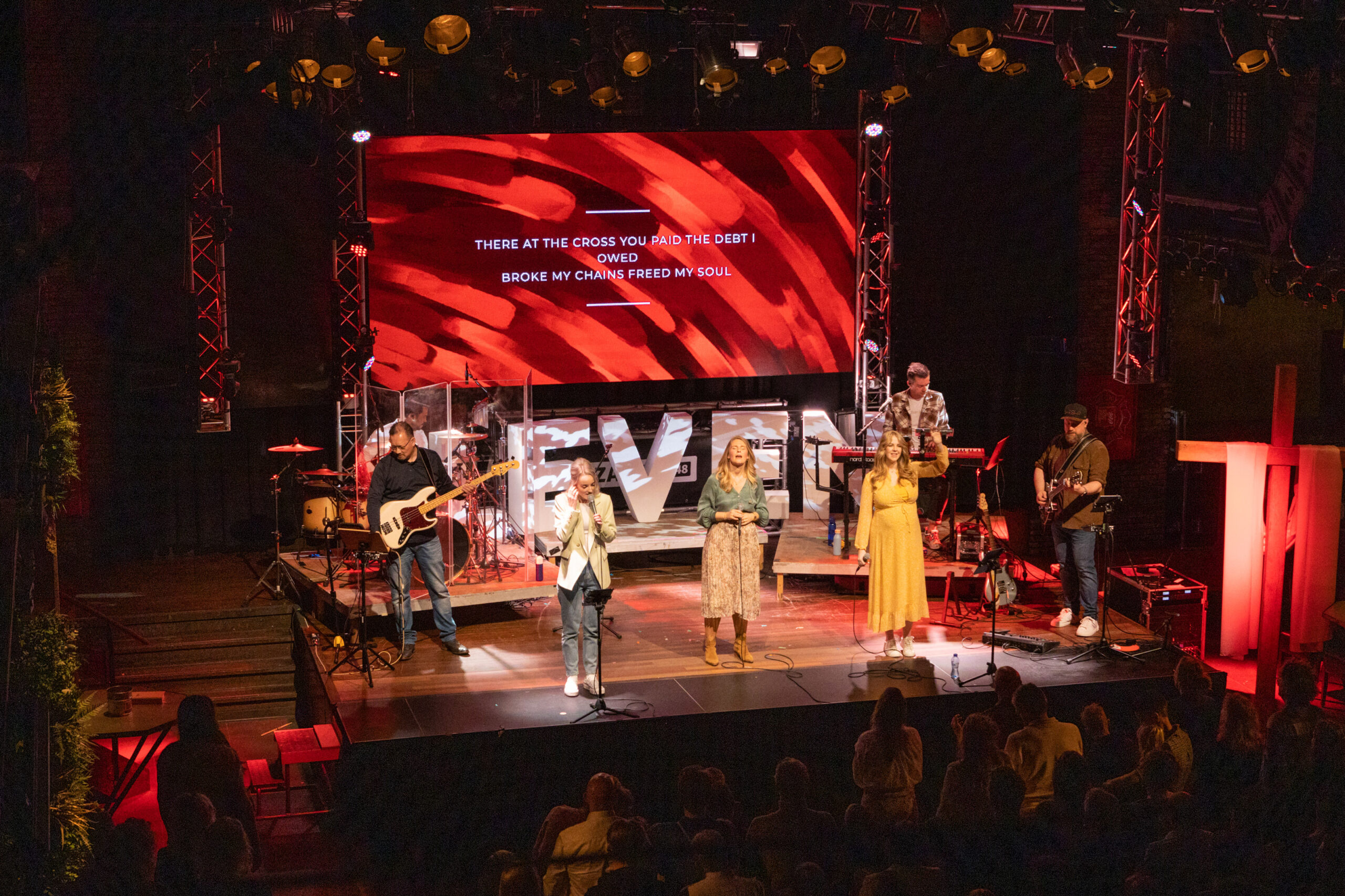 Worshipband met drie zangeressen op het podium van Mozaiek0548 met een rood LED-scherm met songtekst