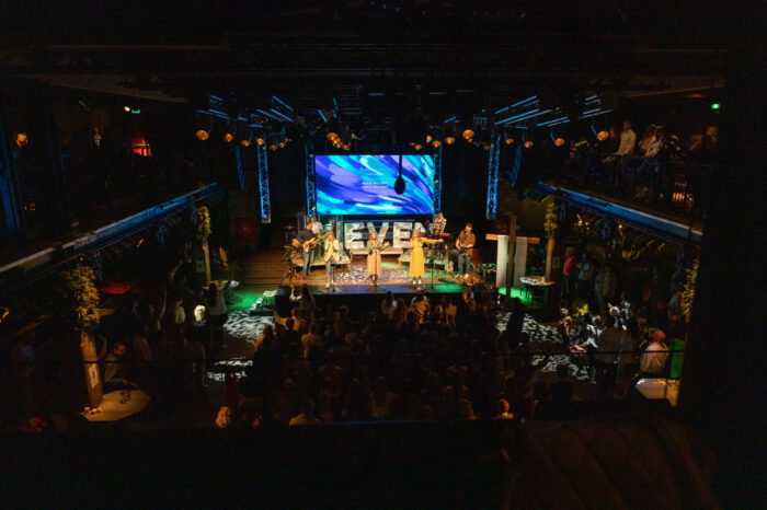 Overzicht van de volle zaal van Mozaiek0548 vanaf de achterzijde, met band op het podium en balkons vol bezoekers