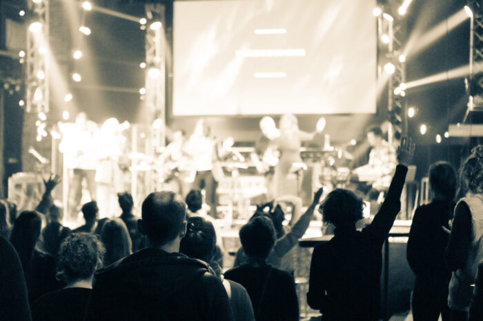 Bezoekers met opgeheven handen tijdens de worship in Mozaiek0548, gezien vanuit de zaal
