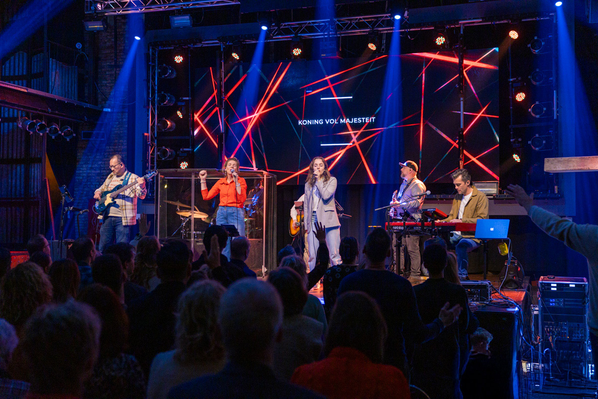 Worshipband speelt tijdens een dienst van Mozaiek0548, met op het LED-scherm de tekst Koning vol Majesteit