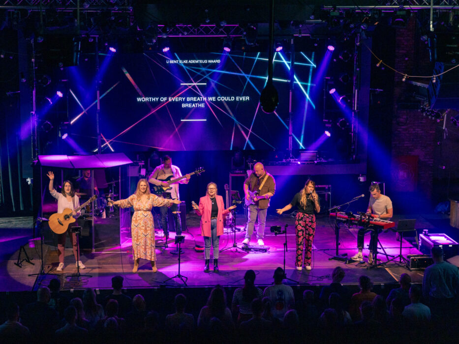 Worshipband van Mozaiek0548 op een roze en paars uitgelicht podium met songtekst op het LED-scherm